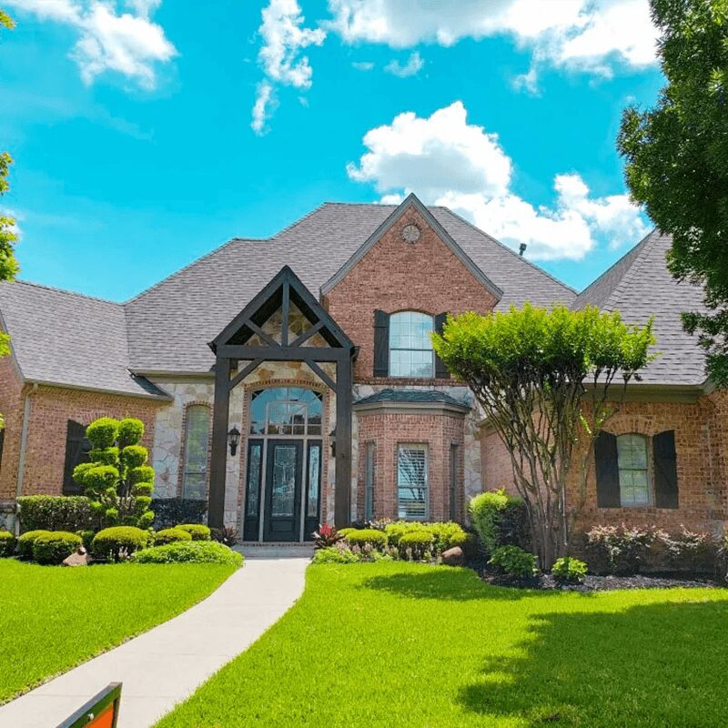 Brick house with green lawn and trees.